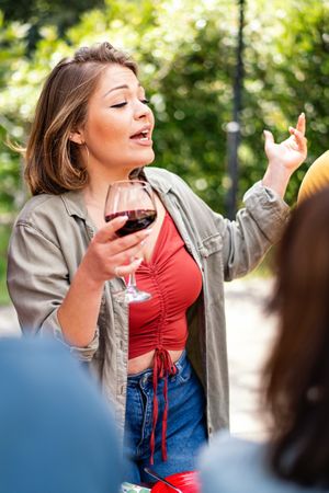 A woman animatedly tells a story during a social gathering, holding a glass of wine