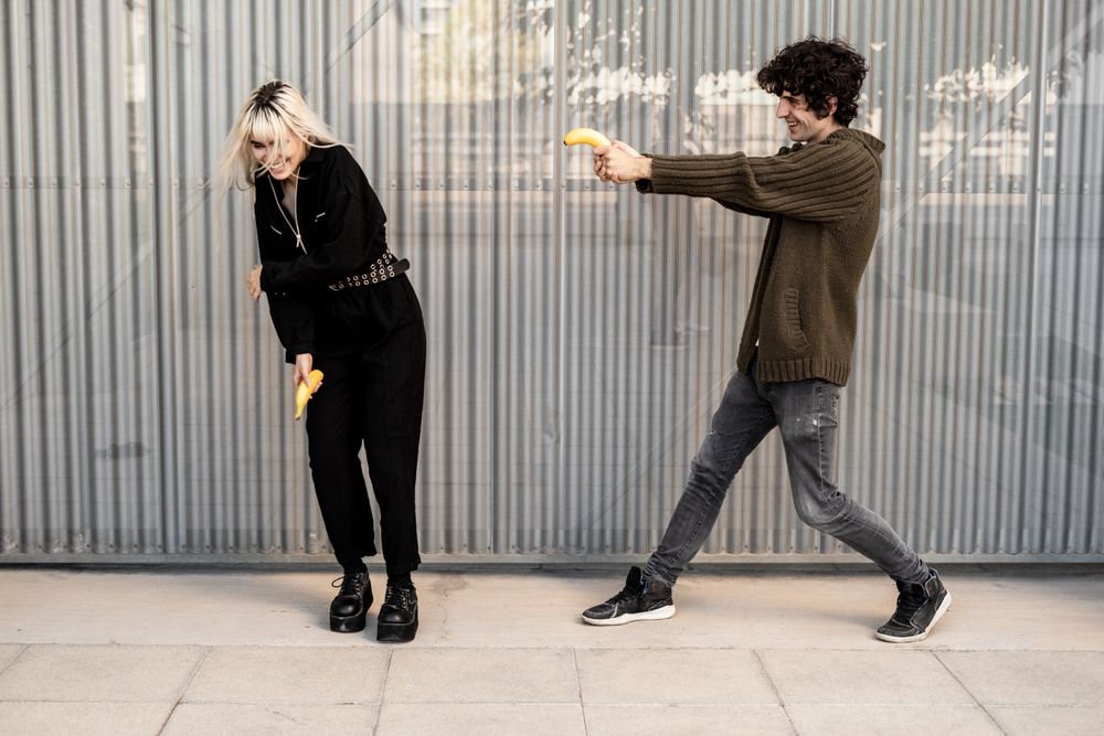 Happy couple pretending to shoot with bananas on street