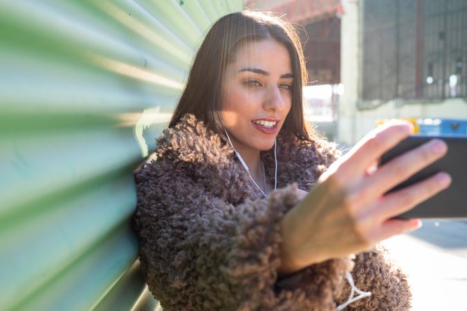 Trendy woman with smartphone near wall