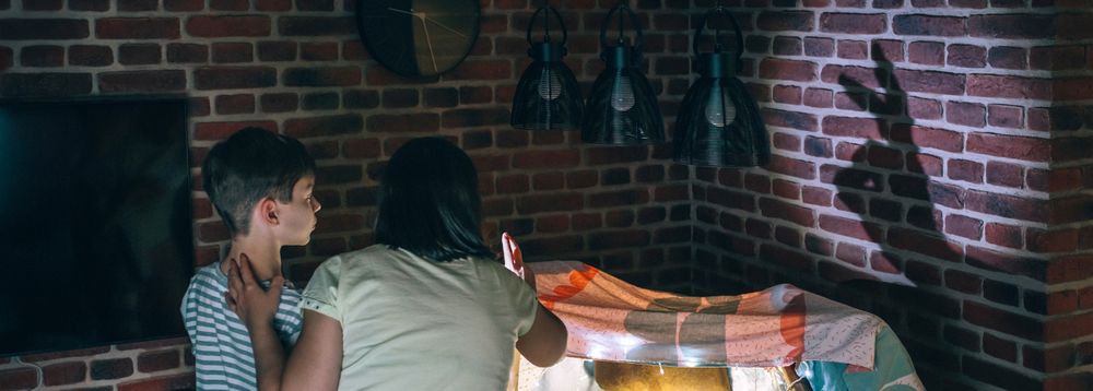 Banner of mother and child having fun playing with shadow puppets over brick wall at home
