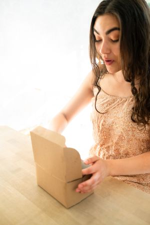 Happy woman in sundress with meal box while sitting at table