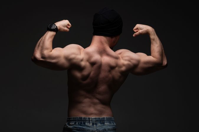 Shirtless man flexing back muscles, powerful pose under moody lighting.