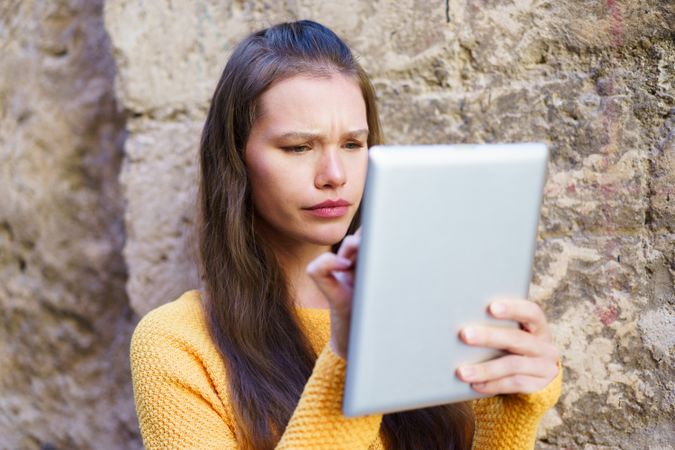 A Young Woman Engaged in Using a Tablet Outdoors, Displaying Strong Focus and Intention