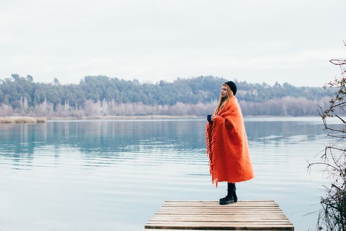 Woman wrapped in blanket on pier of lake