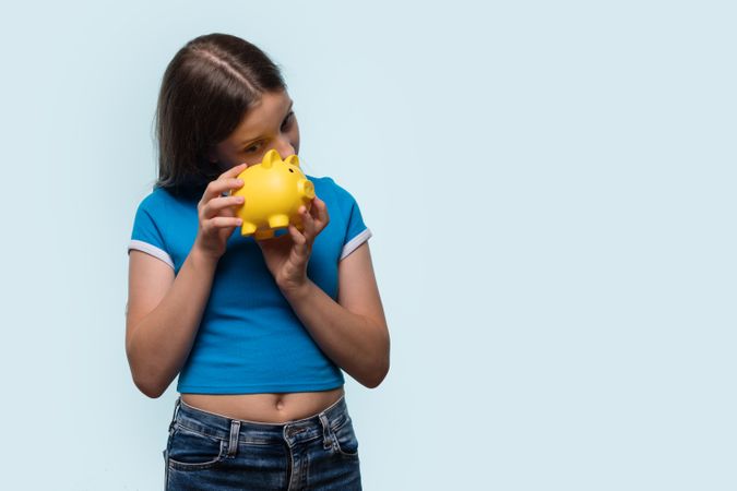 Young girl playfully inspecting yellow piggy bank.