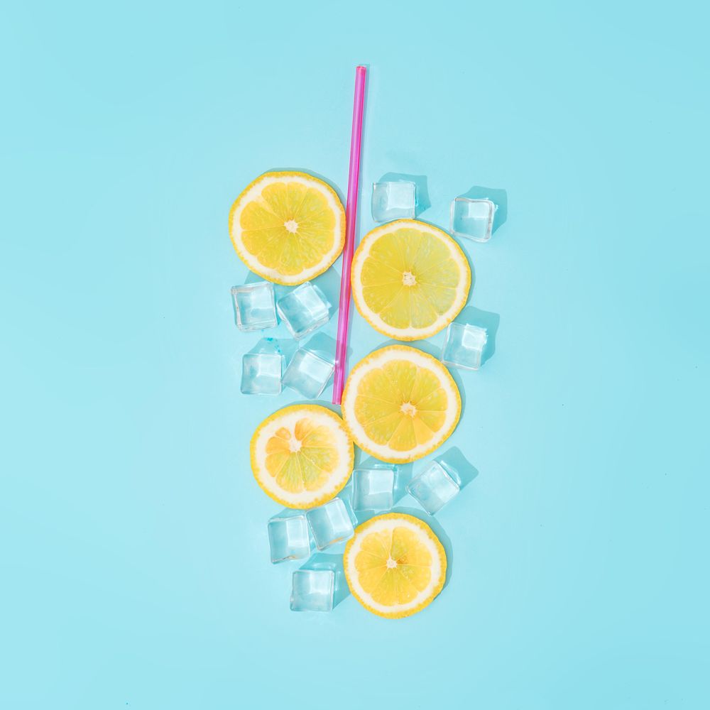 Creative summer background composition with lemon slices, straw and ice cubes