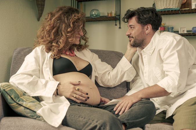 Loving expectant couple looking at each other on the sofa at home.