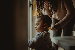 Toddler looking out the window with mother standing behind him