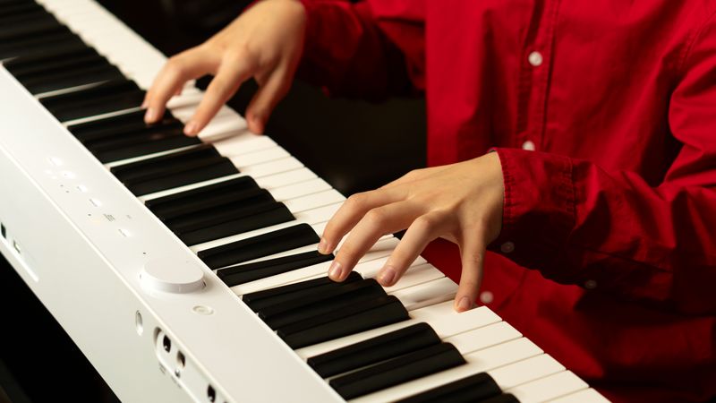 Hands playing white digital piano, fingers pressing keys.