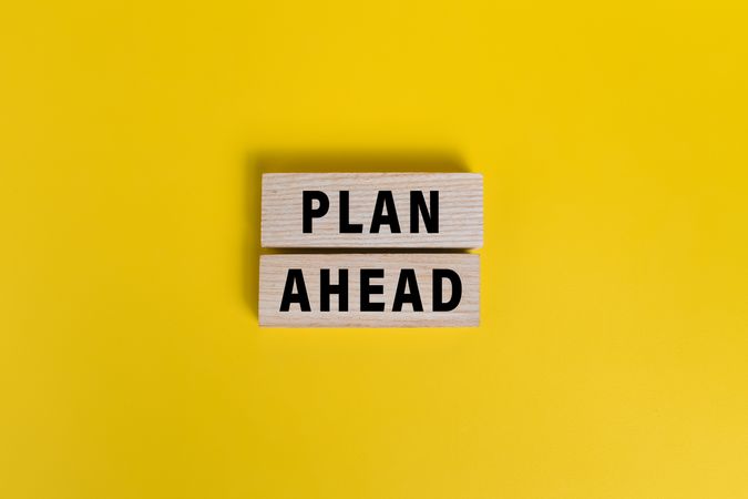 male hand put wooden blocks with plan ahead words isolated on yellow background