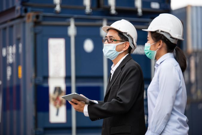 Male and female colleagues on shipping container site in hard hat and face masks
