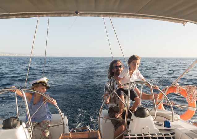 Man with boy and girl holding steering wheel on yacht on water
