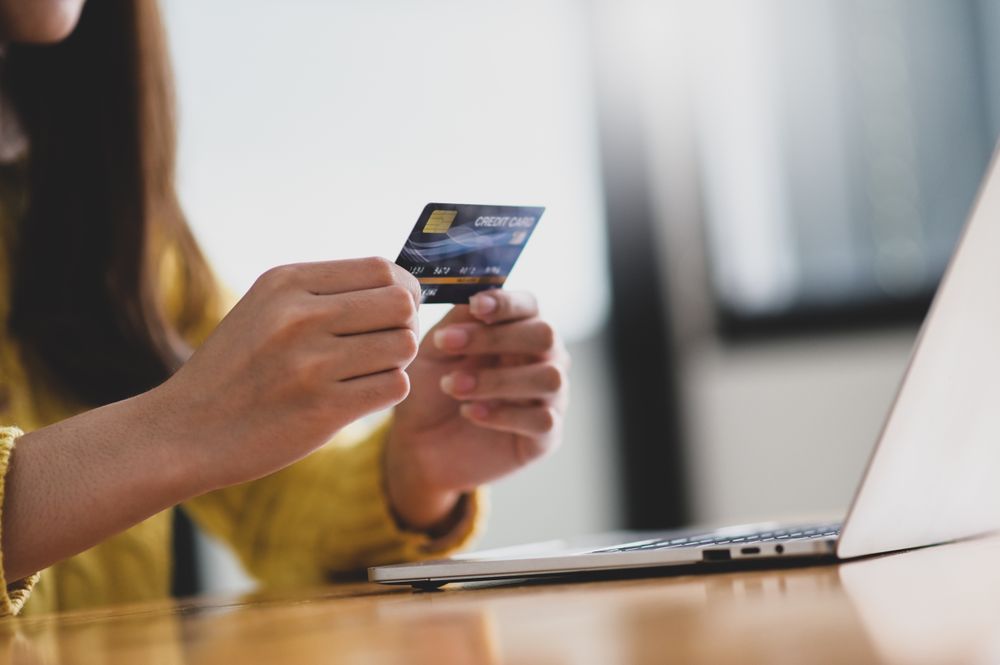 Young woman holding credit card in hand and laptop on the table