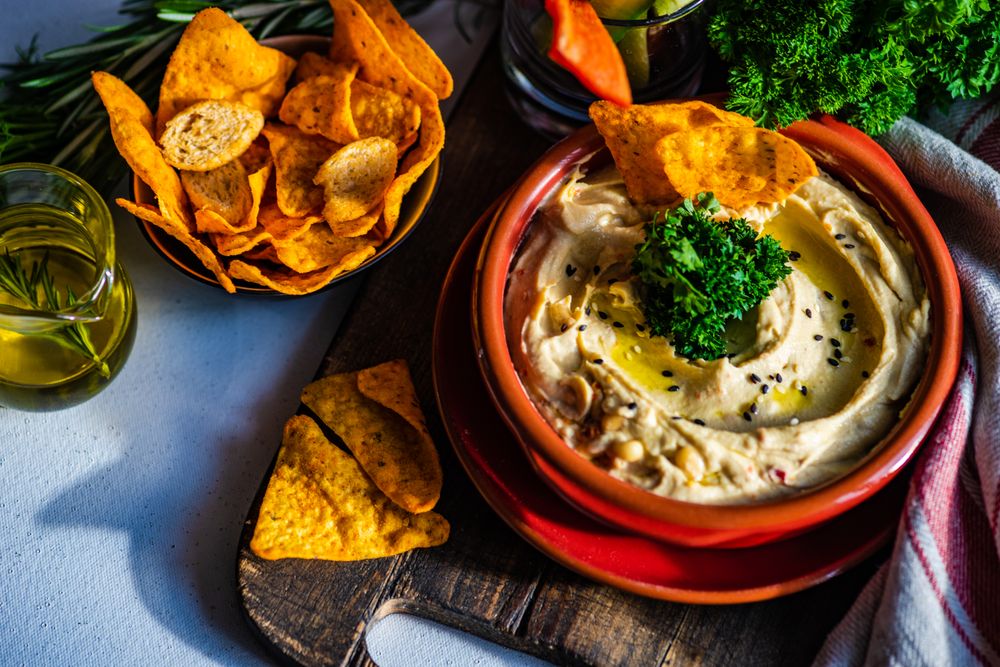 Creamy hummus dip with chips on bread board