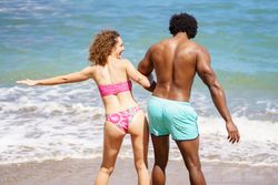 Rear shot of man and woman laughing near the water’s edge at beach