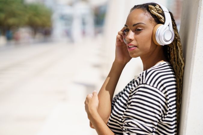 Female leaning on outdoor wall and listening to headphones on sunny day