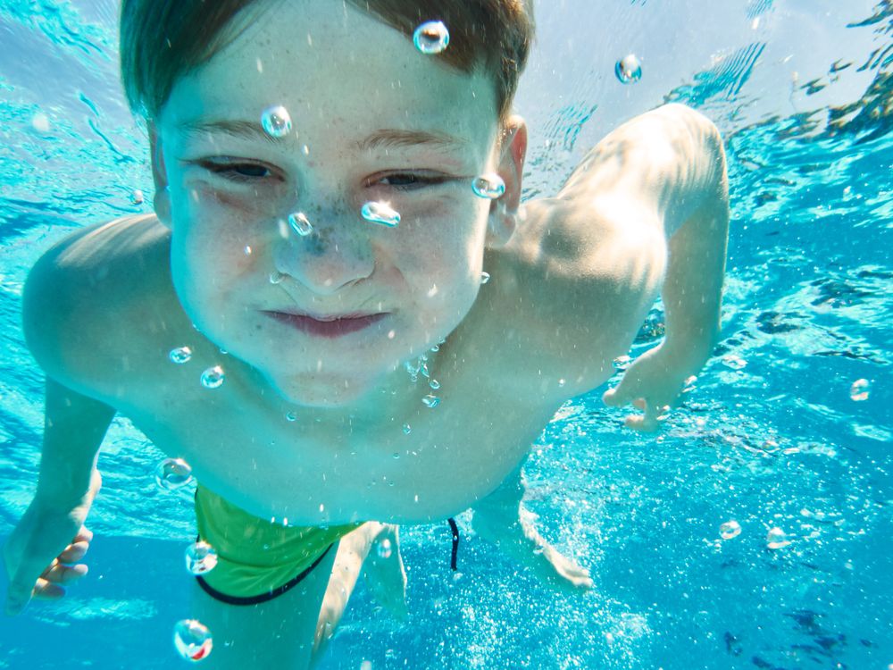 Funny boy swimming underwater looking at camera