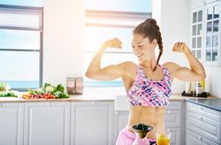 Fit smiling woman flexing her biceps in bright kitchen