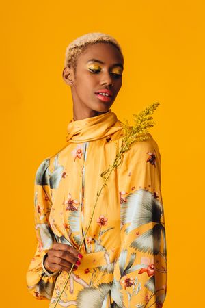 Black woman with short blonde hair holding yellow foliage over shoulders