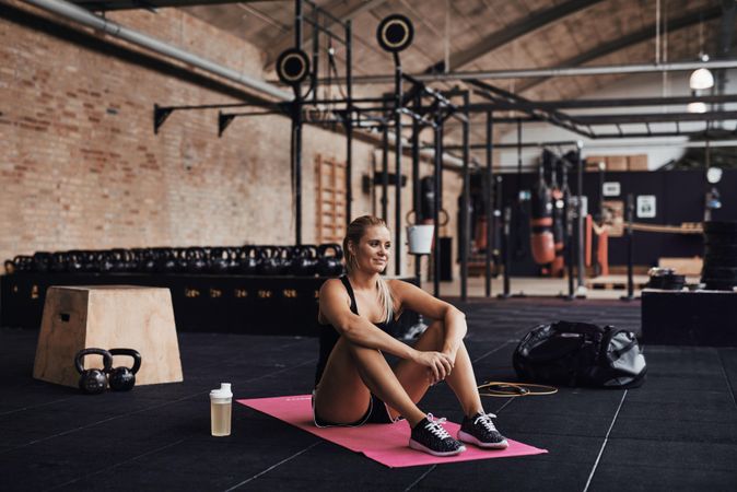 Woman sitting on yoga mat in weights gym