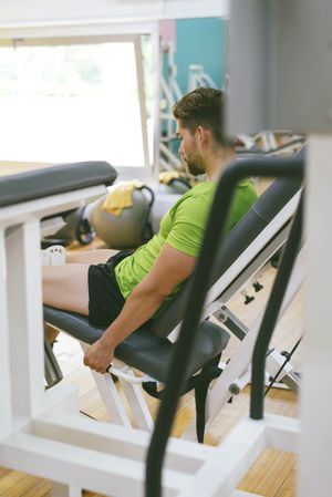 Looking through gym equipment at male in green t-shirt working out using machine, vertical