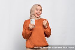 Muslim woman in headscarf and orange shirt celebrating and holding phone 4meYd4
