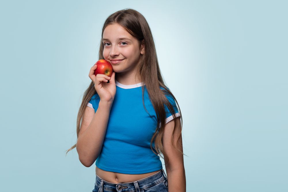Girl holding red apple near face, promoting healthy living.