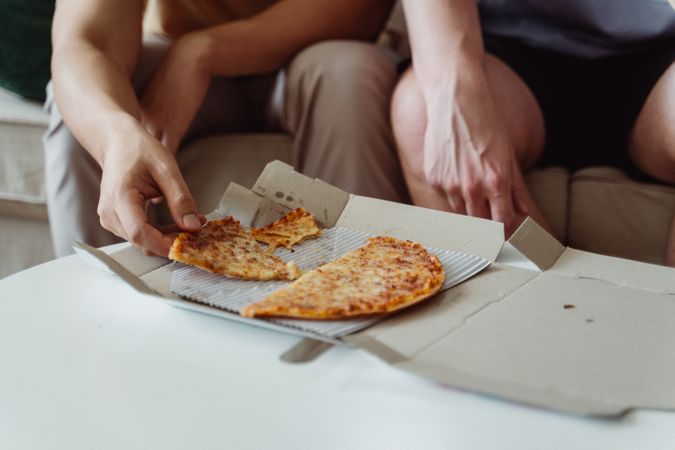 Cropped image of two people eating pizza in living room