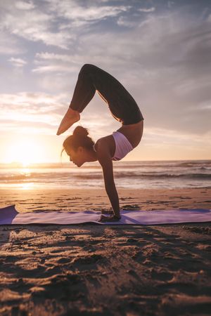 Woman doing yoga asana on the beach at sunset
