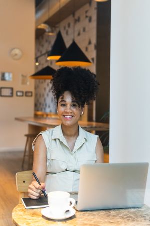 Smiling Black woman working on graphic tablet in cafe
