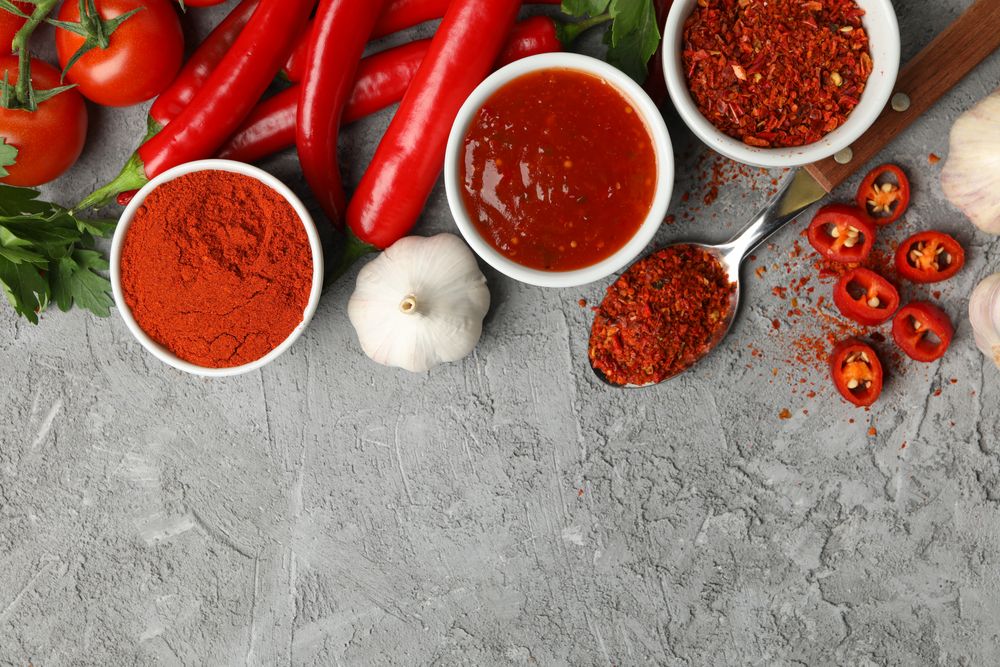 Composition with chilli pepper, powder spice, garlic and sauce on gray background