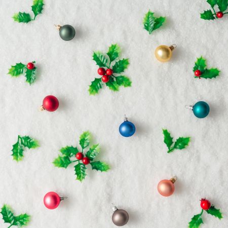 Pattern of plastic holly and baubles on snow background