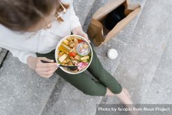 Top view of woman eating a salad sitting on gray steps outdoor 4dMXlb