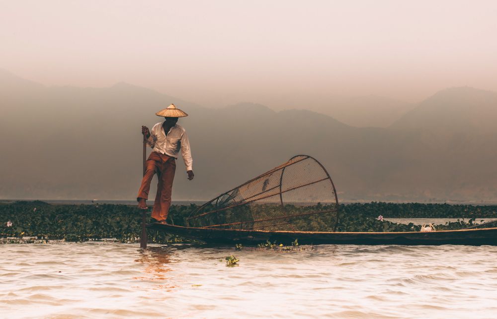 Man with conical hat standing on boat at sunset