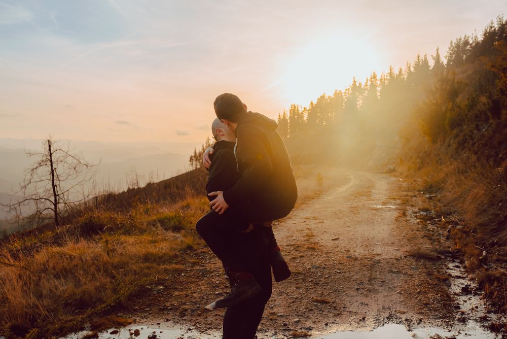 Smiling man holding cheerful guy on road on hill