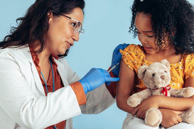 Female doctor giving injection to a girl holding teddy bear