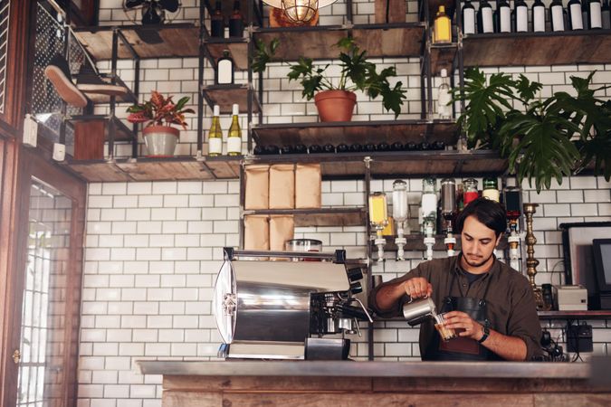 Indoor shot of young male barista making a cup of coffee
