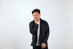 Young Asian Man Standing, Touching Mouth with His Hand