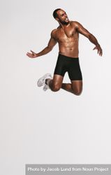 Male athlete jumping in mid air against light background 0VrrN0
