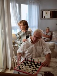Boy near grandfather playing chess at home