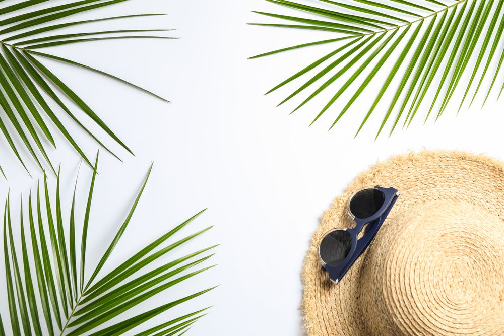 Composition with straw hat, sunglasses and palm leaves on light background. Top view, space for text