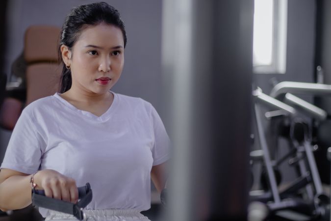 Focused Asian Woman Exercises on Pull Machine at Fitness Center