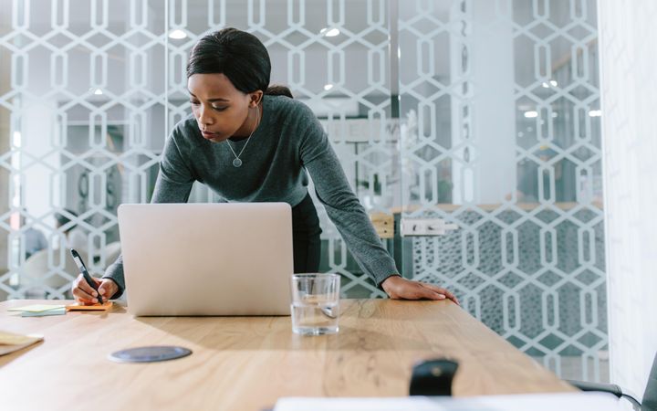 Young woman making notes while working on laptop in office boardroom