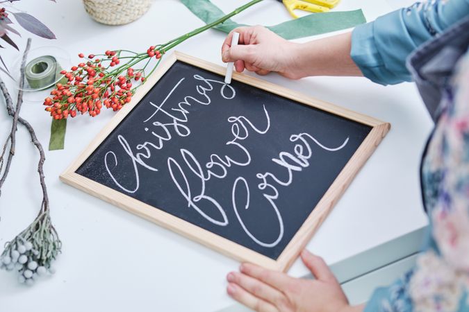 Crop woman writing on board with chalk in flower store