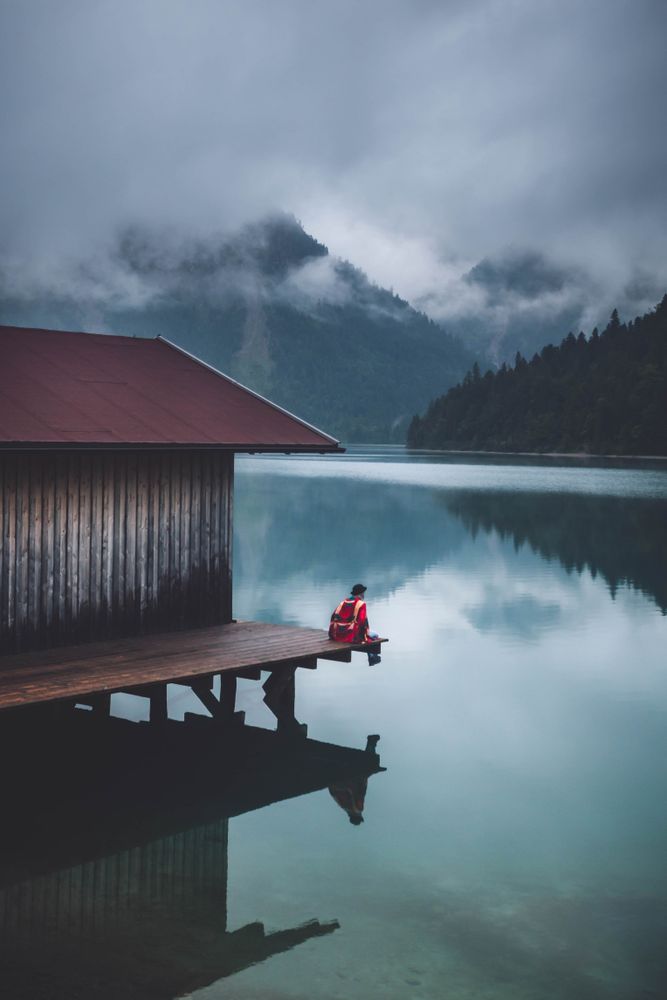 Person sitting on dock over lake under cloudy sky