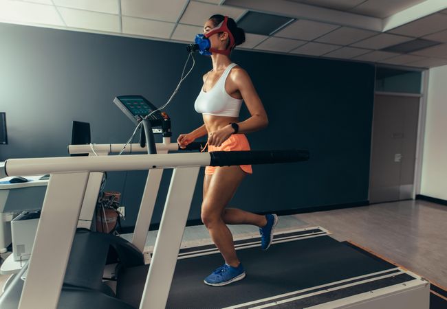 Female runner with mask running on treadmill machine testing her performance
