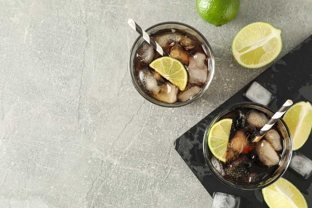 Glasses with cold cola and citrus on grey table, top view