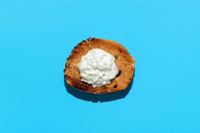 Tzatziki sauce on a toasted bread slice, isolated on a blue background