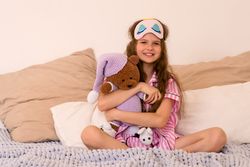 Young girl hugging teddy bear while sitting on bed.