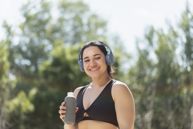A young girl smiles while drinks water to hydrate herself, from a reusable bottle, during a morning exercise session